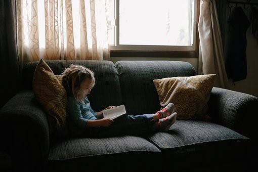 A little girl sitting on a sofa reading a book
